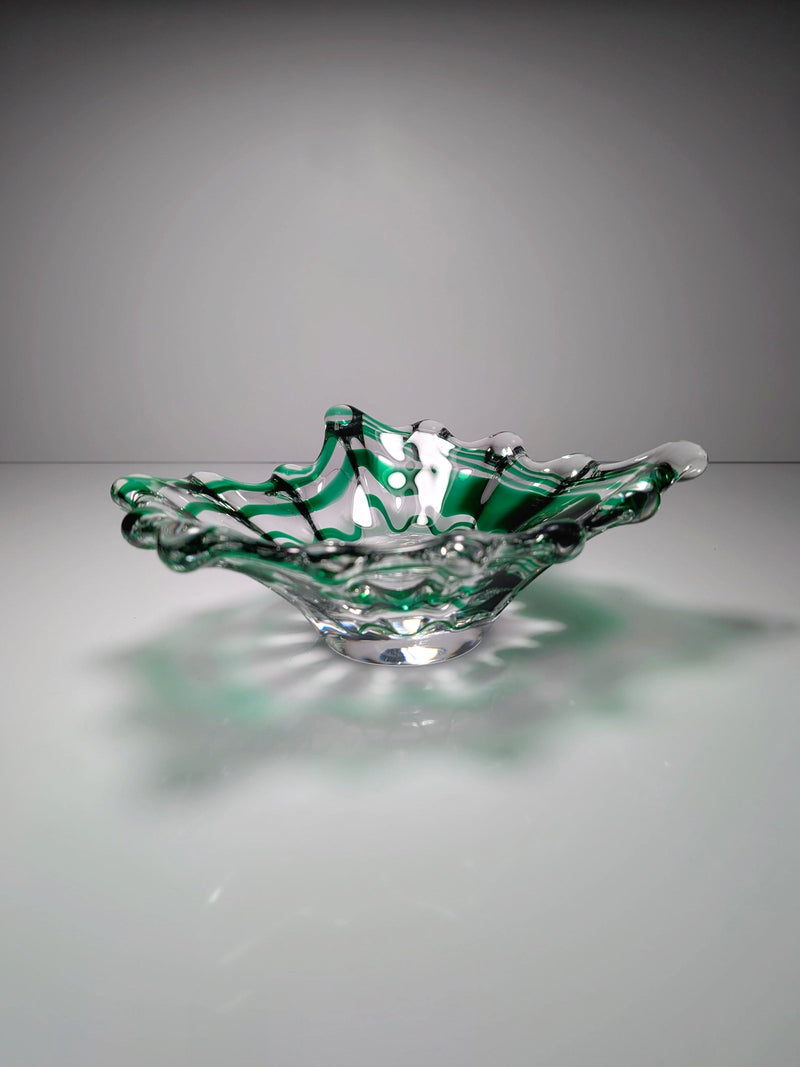 The Green Swirled Murano Vide-Poche by Dodo Vintage features wavy, ruffled edges and vibrant green streaks, evoking the elegance of a classic Murano piece as it rests on a reflective surface under soft lighting.