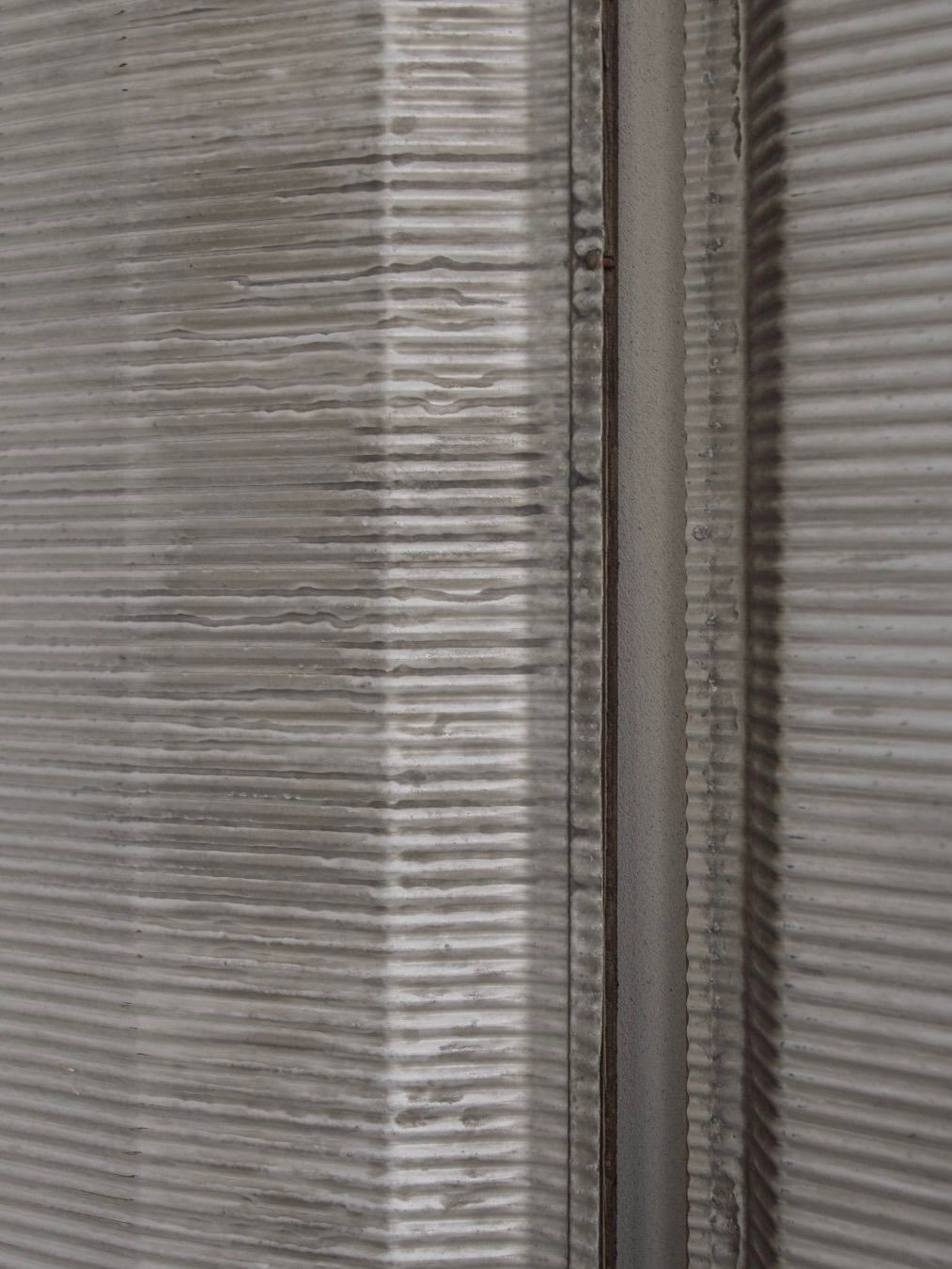 The Jean Prouvé - Façade Panel 70 by Bicci de' Medici features a textured, ribbed gray metal surface with vertical ridges. The overlapping panels create a narrow center gap, showcasing embossed aluminum details with subtle tonal variations, reminiscent of Prouvé's industrial style.