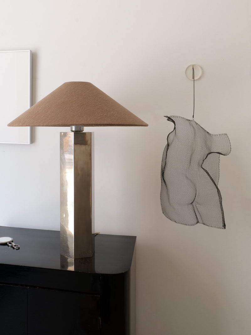 A modern living space features a metallic geometric table lamp with a beige shade on a black console, complemented by the Collection apart 'Turning Torso' wall sculpture. The minimalist decor is highlighted with Swedish-inspired design and neutral tones.