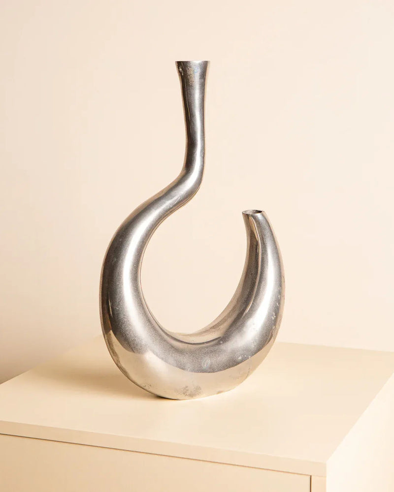 The Vase "Ondule" in Aluminum 80's by Treaptyque, featuring a modern abstract twisted design, rests on a beige surface with a matching background, capturing the sleek essence of Milan design.