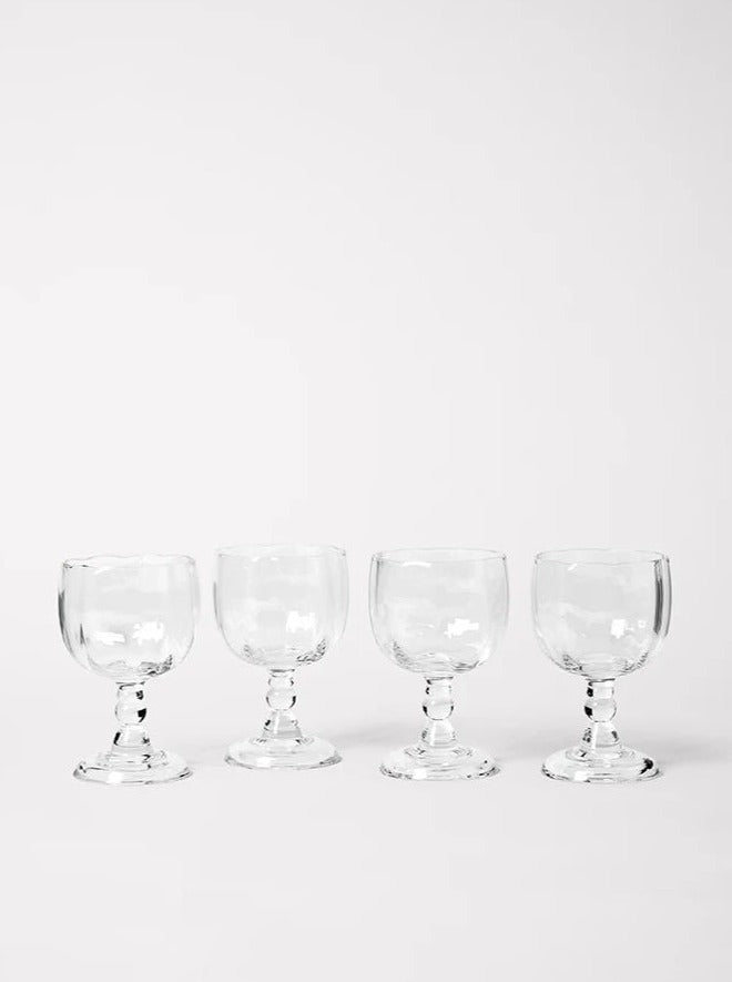 Four empty Alban Wine Glasses from Akua Objects arranged in a straight line on a white background, showcasing their transparent and elegant design.