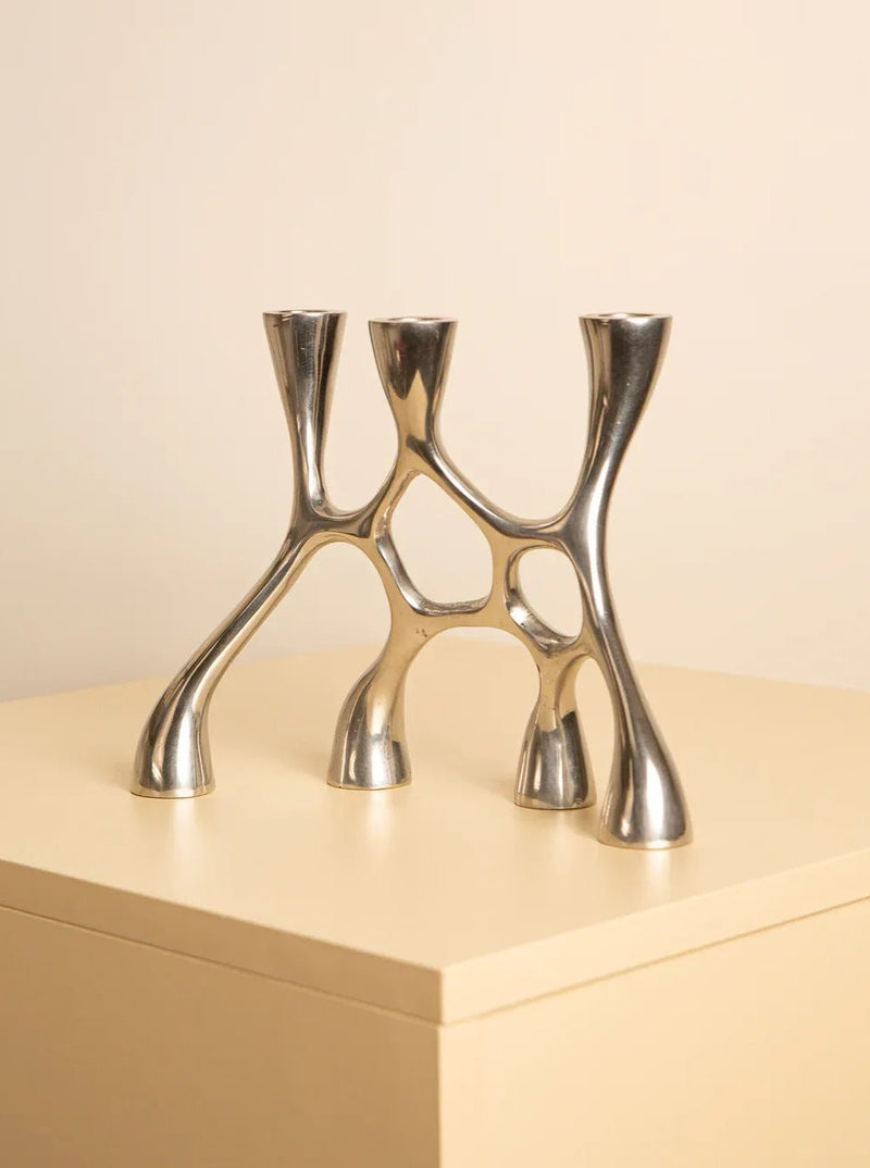 A modern, metallic Treaptyque 80's Aluminum 4-head Candleholder with a unique, branching design, displayed on a beige surface against a light beige background.