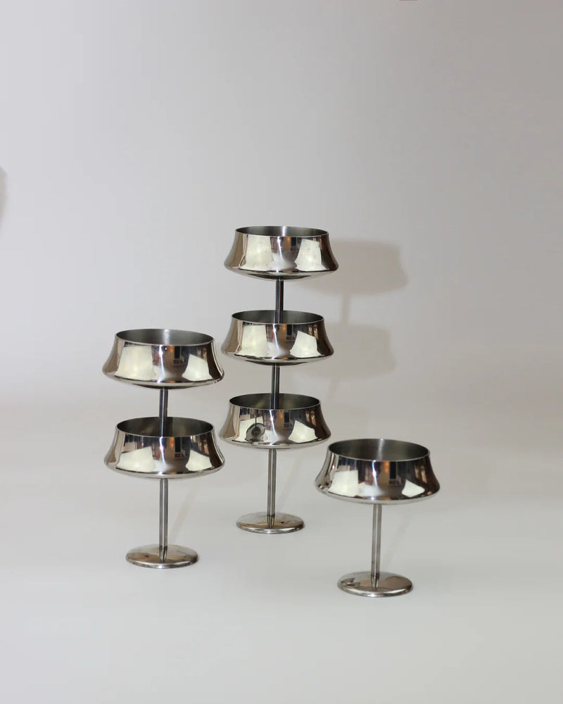 Six stainless steel cups from Boga Avante Shop are arranged in a staggered formation against a light background. Perfect for serving fruits or desserts, each cup features a round base and a shallow, wide bowl.
