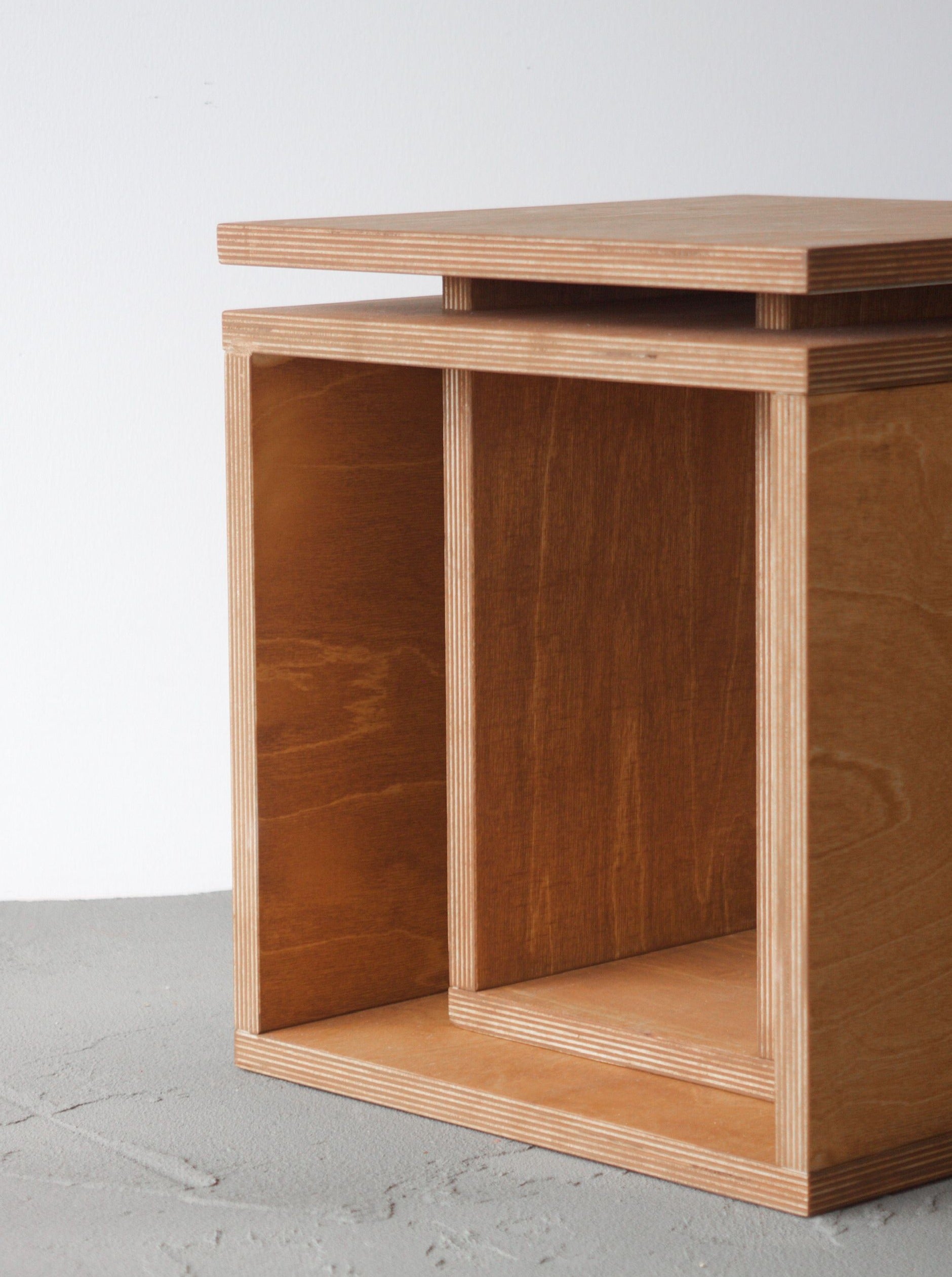 A minimalist Cubo side table from Edoardo Lietti Studio with an open shelf and a smooth top, featuring visible wood grain and clean lines, set against a neutral gray background.