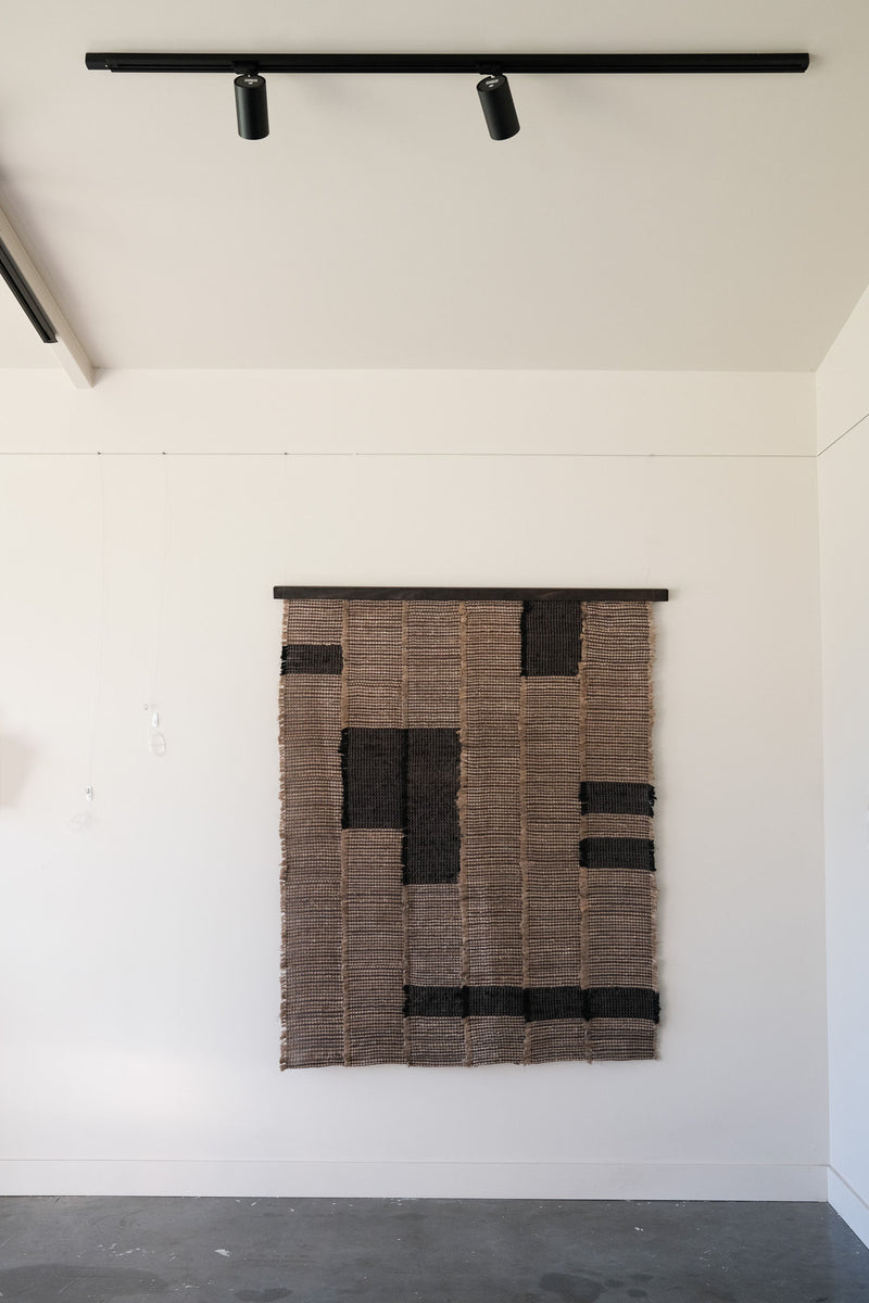 Handwoven textile wall sculpture with geometric black patterns on natural fiber