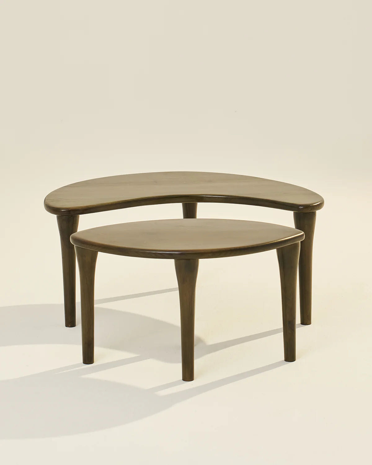 The LMNOH Crescent Coffee Table set features two space-saving ashwood tables: a smaller circular one partially nested under a larger crescent-shaped table. They both have a smooth, polished finish and are displayed against a neutral background.