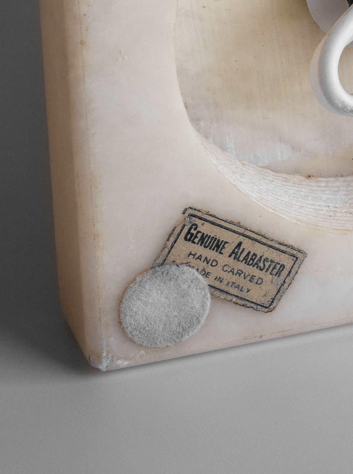 Close-up of the corner of a White Knight Alabaster Table Lamp, handcrafted by Spigel in Italy during the 1970s, featuring a label that reads "Genuine Alabaster, Hand Carved, Made in Italy." The corner displays a felt pad beneath the label for protection.