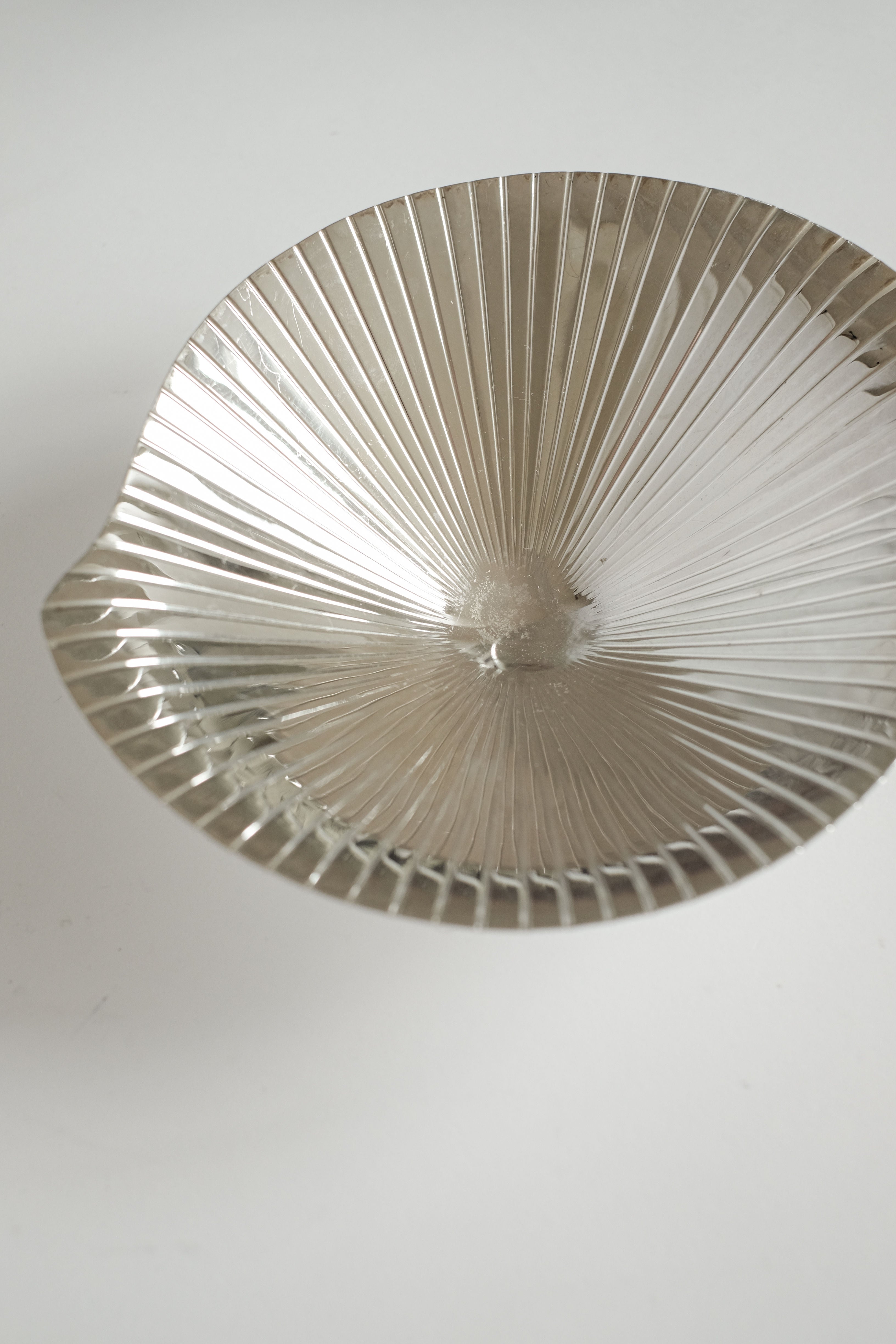 The Silverplated Shell Dish WMF by septembre studios features a metallic, fan-shaped bowl with a ridged texture on a light surface. Its vintage appeal is captured through its glossy silverplated design and dynamic wavy edges that reflect light beautifully.