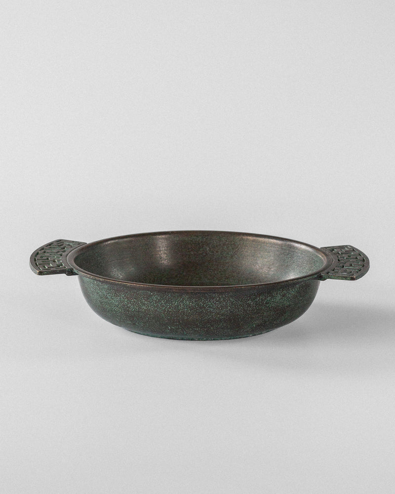 The Spigel Art Deco Bronze Bowl, from 1930s Sweden, is a round, texturally charming pot with dark green metal and ornate Greek key handles on each side, placed on a plain white background.