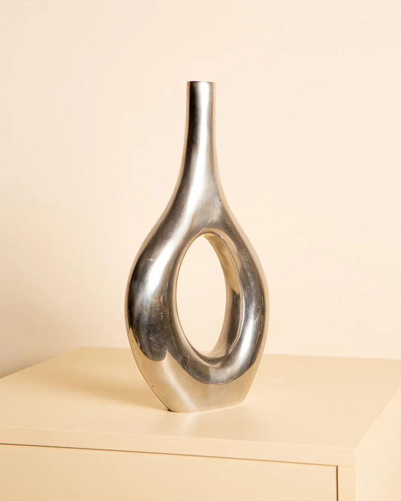 The Treaptyque "Long Italian Vase in Cast Aluminum 80's" from Northern Italy, featuring a sleek oval opening, elegantly rests on a cream-colored surface against a light beige backdrop.