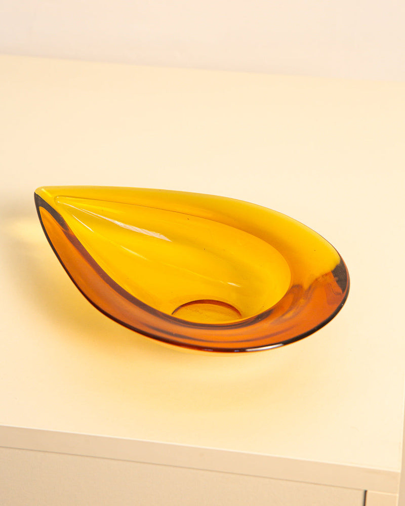 The Large Italian Vide-poches "Poire" 60's by Treaptyque, a yellow and amber teardrop-shaped glass bowl inspired by 1960s Italian design, rests on a light surface with a neutral background.