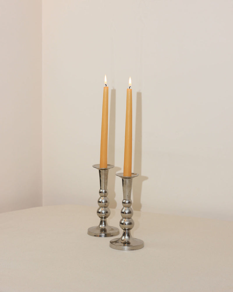 Two polished chrome Acero candleholders with lit taper candles