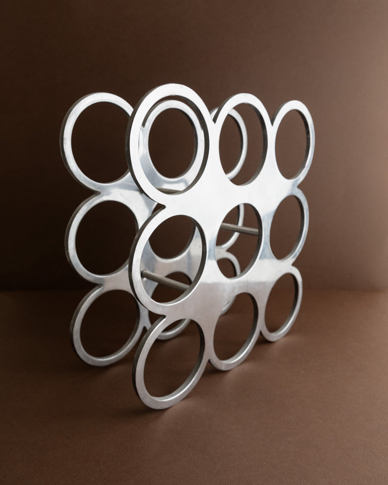 A stylish wine rack from Bottega Jacobs, featuring a retro 1970s interlocking circular design, is placed against a brown background. This vintage metal piece can hold up to nine bottles in a horizontal position and offers an eye-catching space age design perfect for both storage and decoration.