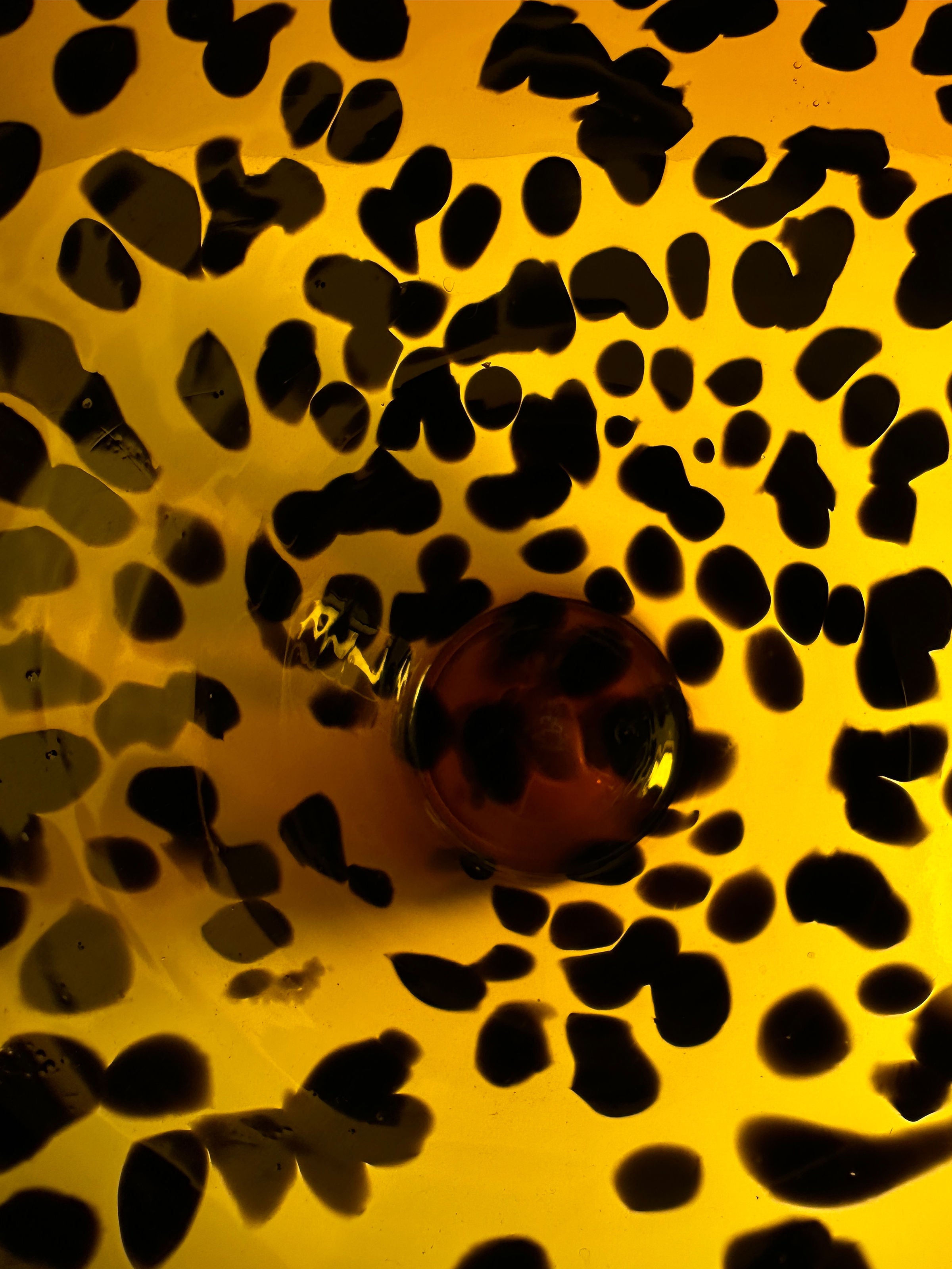 A close-up image features a Tortoise vase Murano for Christian Dior from the 1960s, with a yellow background highlighting its irregular black and dark brown spots. At the center, a glossy, deeper brown circular shape enhances this design's depth and elegance, brought to you by Dodo Vintage.