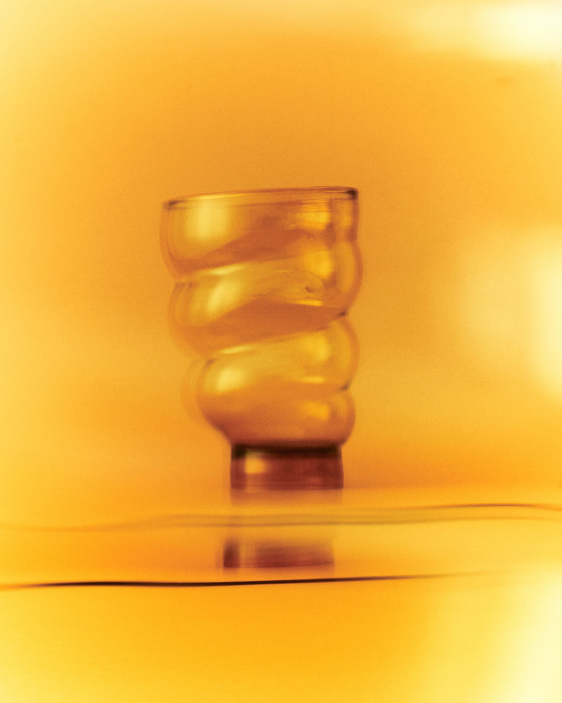 The 'Paguro' Amber Glass by Ylaria Pavone rests on a flat surface, glowing with warm orange-yellow light—an exquisite, handcrafted glass decor piece that brings a soft, dreamy ambiance to any space.