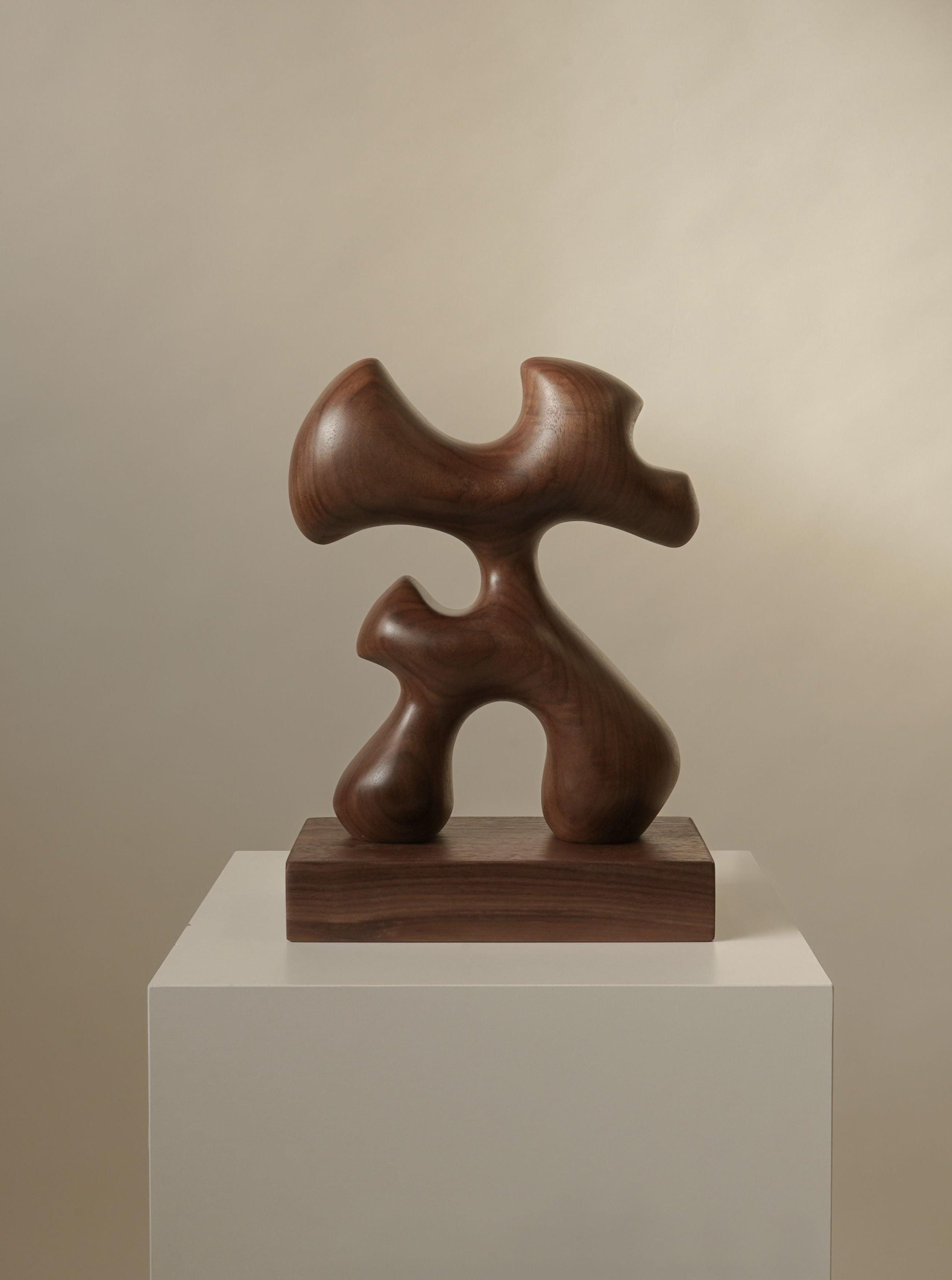 Abstract Abari wood sculpture with fluid, interlocking shapes, displayed on a white pedestal against a neutral beige background by Chandler McLellan.