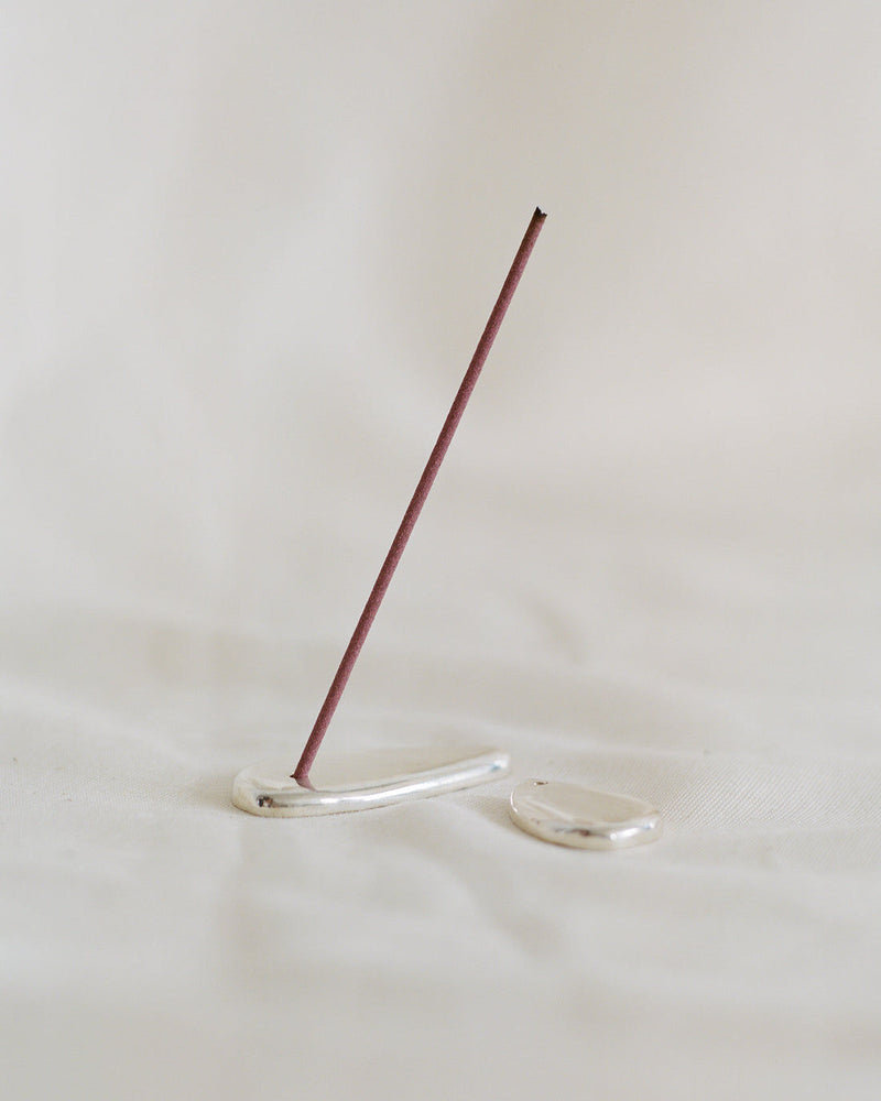 Sterling silver incense holder with lit incense stick on white surface