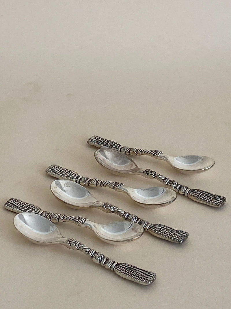 Five Aesthete Label French Tassel Spoons with intricately designed, textured handles are arranged casually on a light beige surface. The silver-plated spoons, in excellent vintage condition, feature a unique pattern resembling braided or woven metal. Reflecting light softly, they suggest a polished finish—perfect for a decorative table setting.
