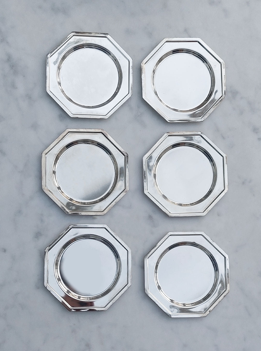 The Set Of 6 Coasters by Les Objoies, featuring octagonal designs with glossy reflective surfaces and crafted from durable material, are arranged in two vertical columns of three on a white marble background.