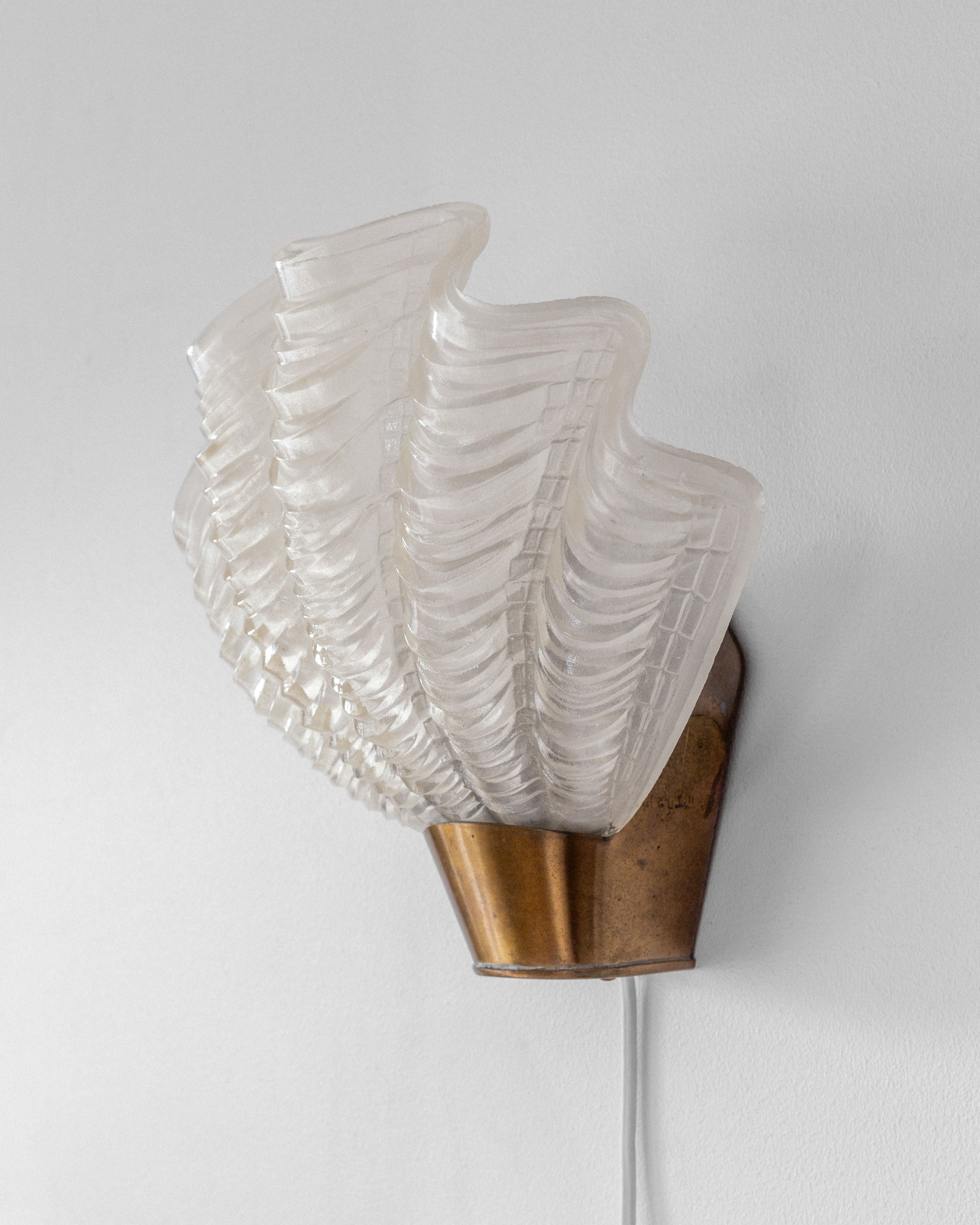 The Vintage "Coquille" Wall Light by Spigel, from 1940s Sweden, features a brass holder and a fan-shaped translucent glass design. Mounted on a plain white wall, it beautifully merges classic and contemporary styles.