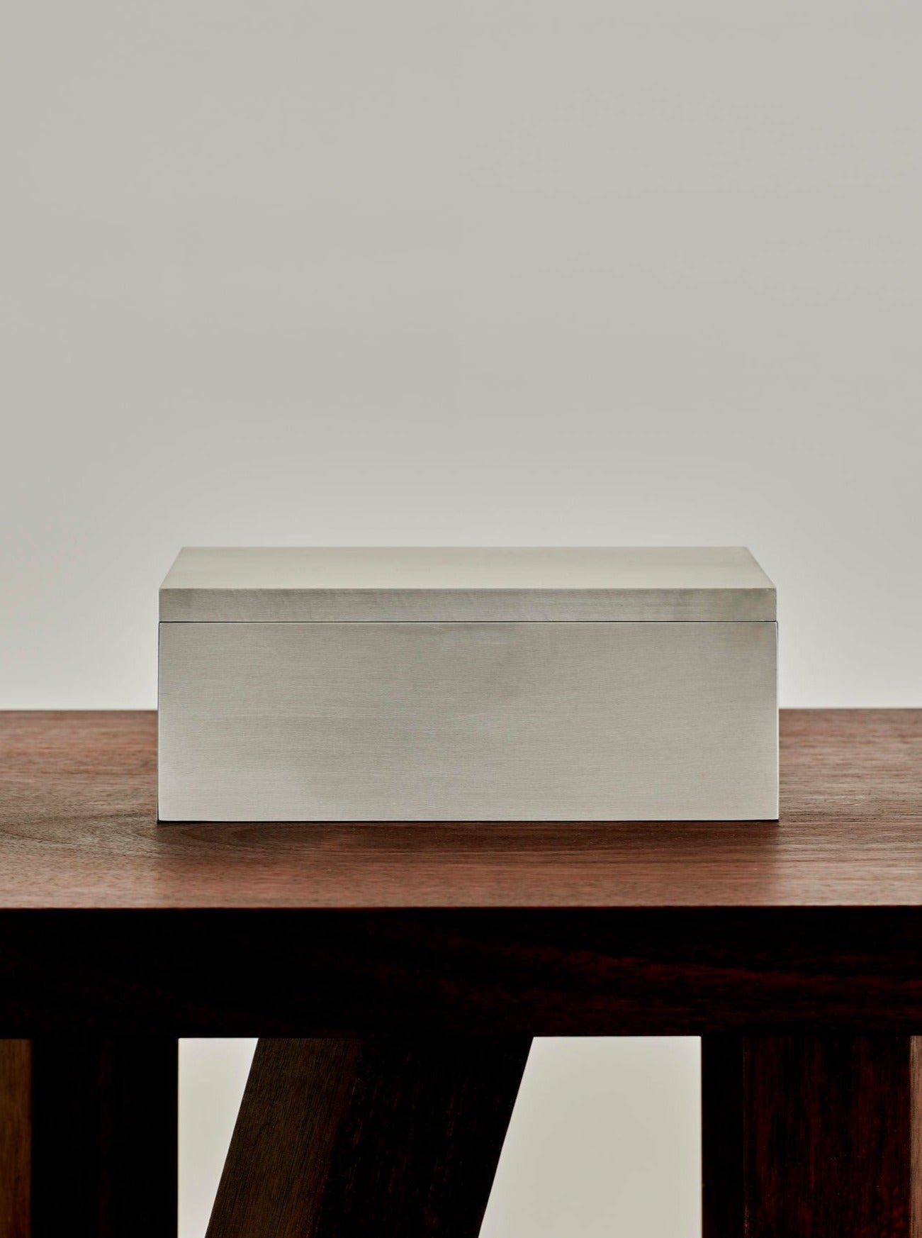 A MOCK STUDIO Miter Box is placed on a wooden table against a light grey background. The table has a rich, dark finish with distinctive angled legs.