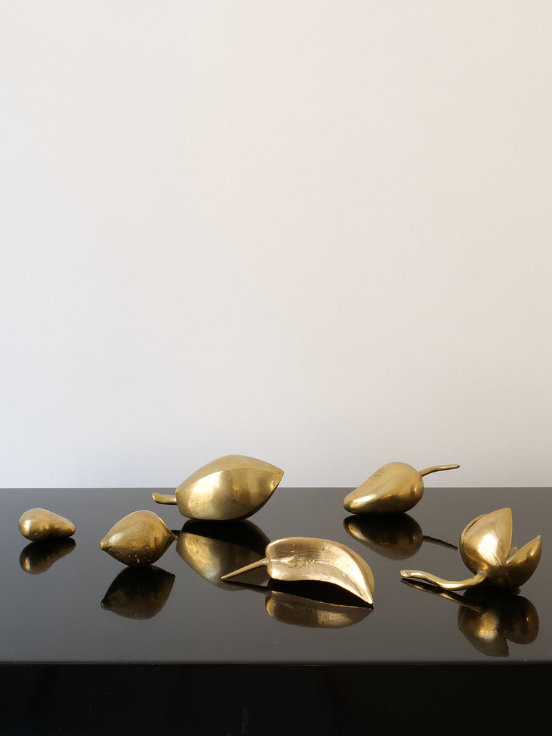 A mesmerizing arrangement of midcentury, leaf-shaped sculptures in a gold hue from the "Brass Sculpture Collection" by Collection Apart is displayed on a glossy black surface, capturing and reflecting the light brilliantly. These solid brass pieces are strikingly showcased against a simple white backdrop, highlighting their elegant metallic design.