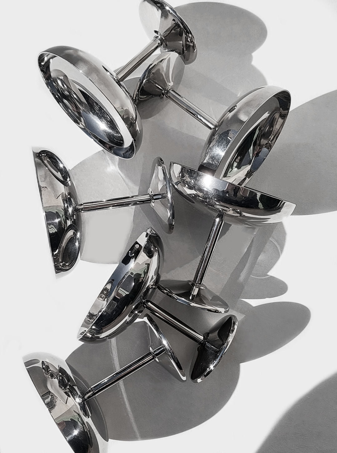 A set of 6 shiny, stainless steel ice cream cups from Les Objoies are displayed upside down on a white surface, casting soft shadows. The cups have smooth, reflective surfaces, creating a modern and elegant arrangement.