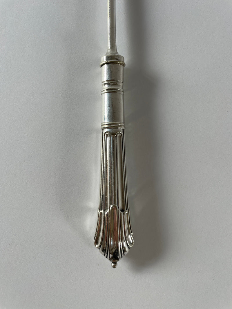 Close-up of the intricately designed handle of a Maud Vaughan Antique Silver Plated Bread Fork against a plain white background. The ornate handle, reminiscent of Victorian etiquette, features a fluted pattern and a small, rounded finial at the end. The elegant design underscores its identity as part of an exquisite decorative household item.