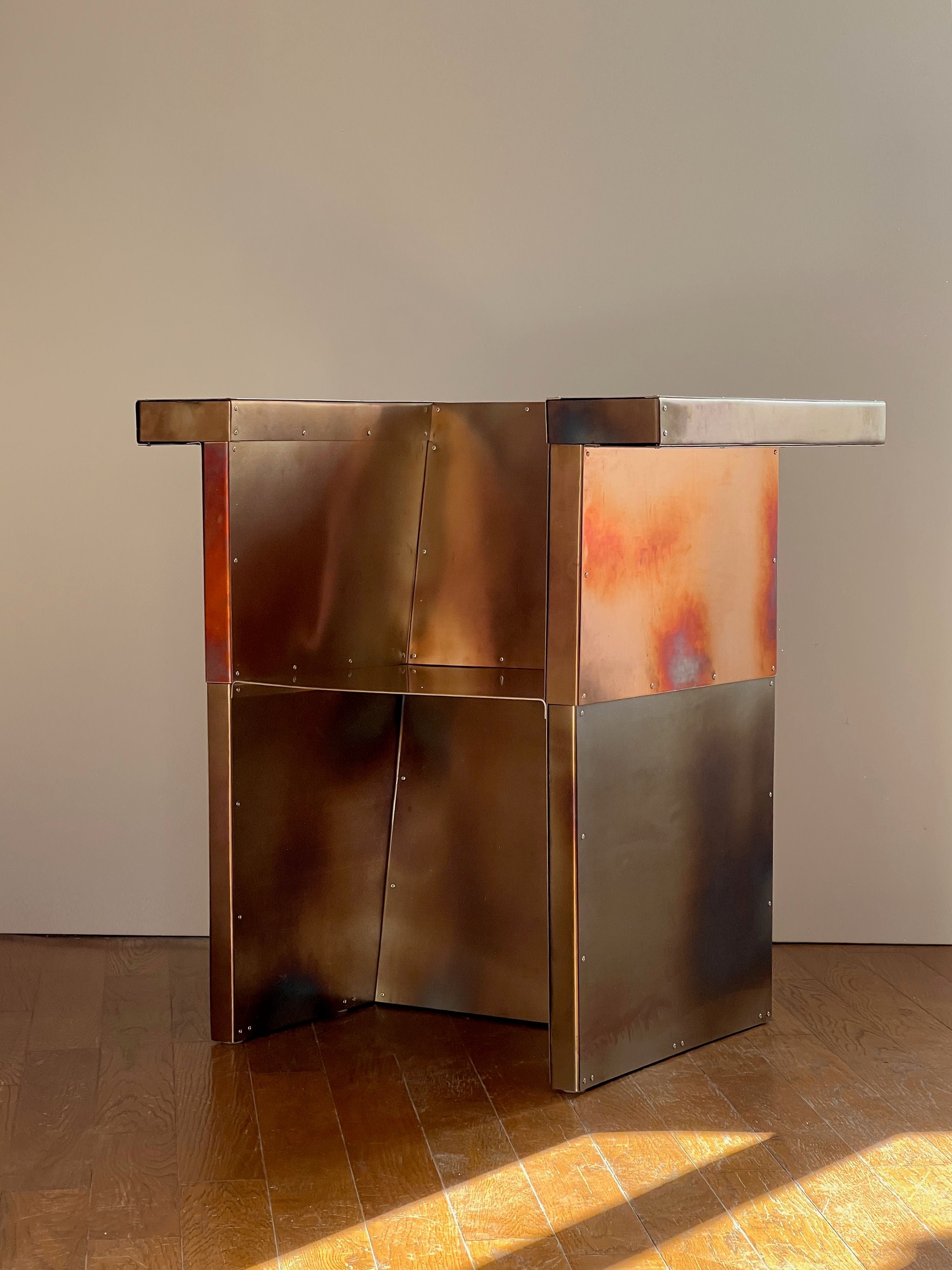 The Throne desk by Theo Galliakis features industrial rivets, geometric panels, and a bronzed finish with orange accents, bringing modern angular style and custom-made appeal to any room.