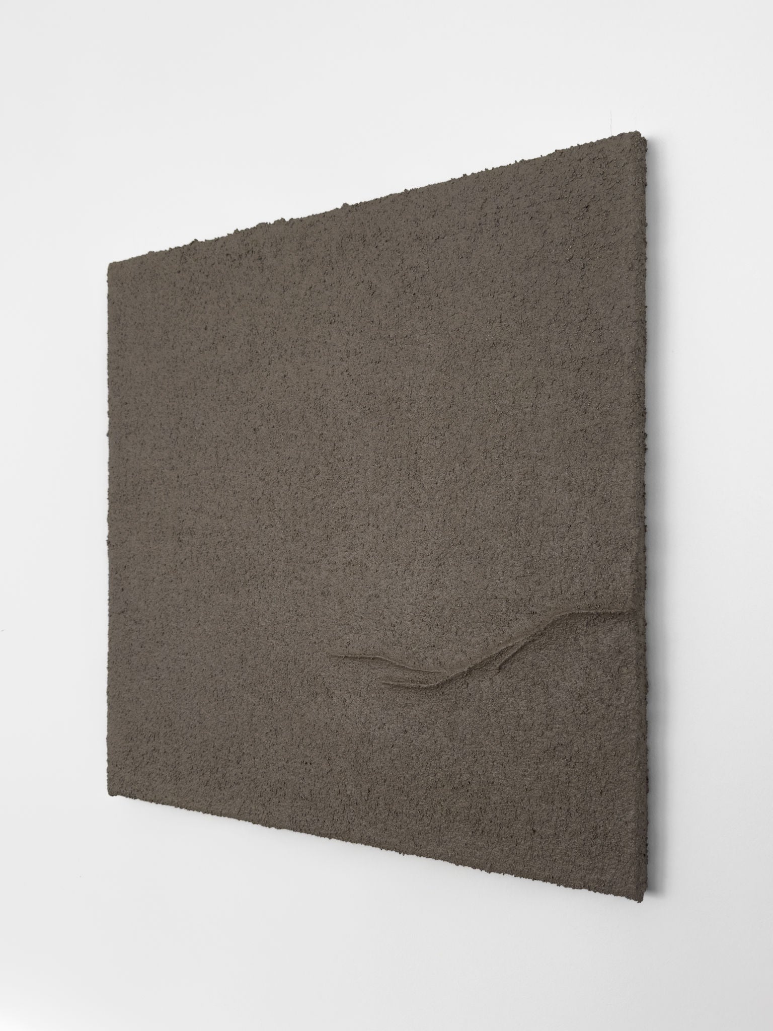 Shadow World 04" by Delal Salazar, a textured, rectangular gray-brown canvas made with acrylic and sand, features a single raised curved ridge near the bottom right and hangs on a white wall.