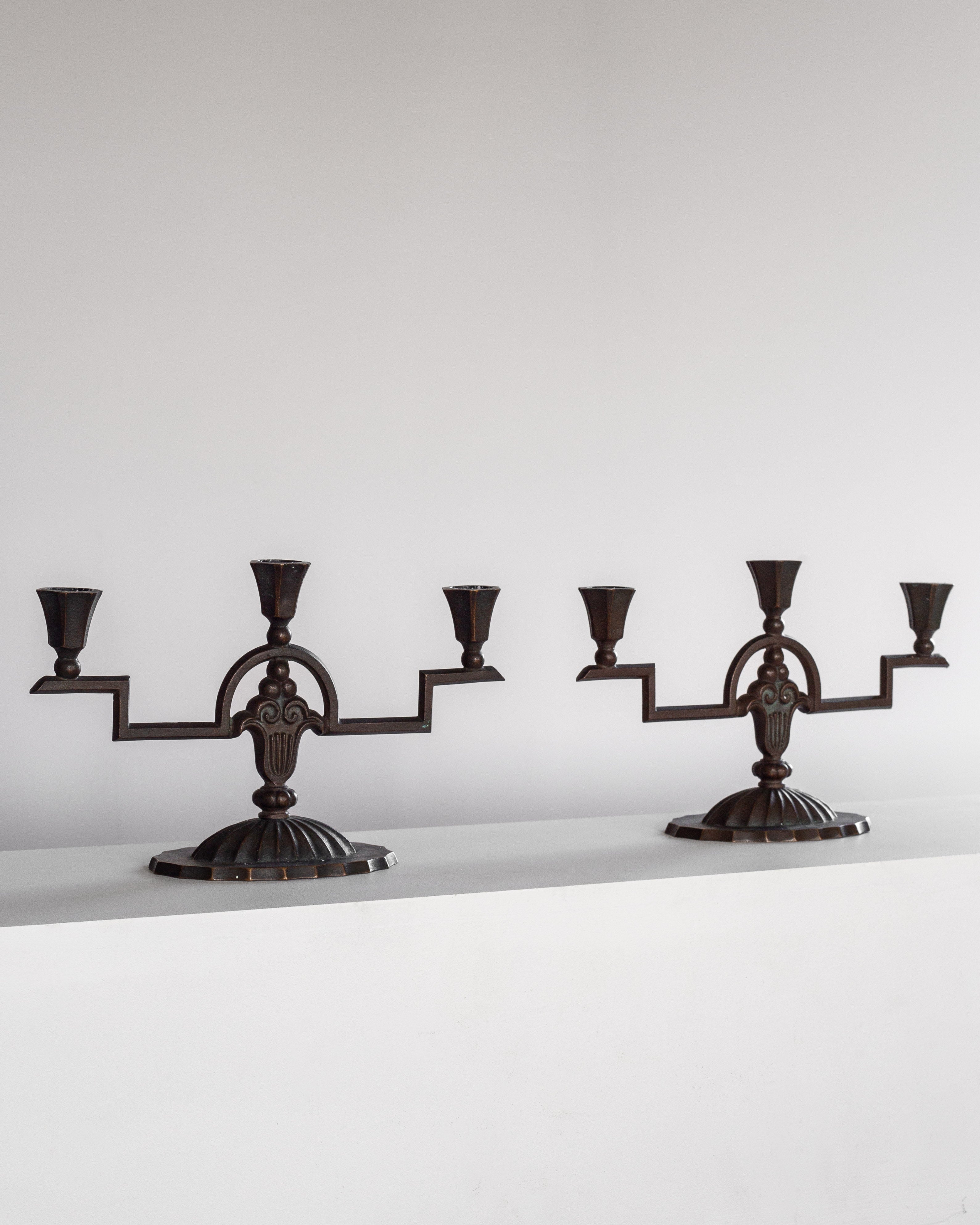 Two Spigel Art Deco Bronze Candelabras from the 1930s, featuring symmetrical, stepped arms and ornate central designs, are displayed side by side on a plain white surface against a white background. Each solid bronze candelabra holds three candle holders.