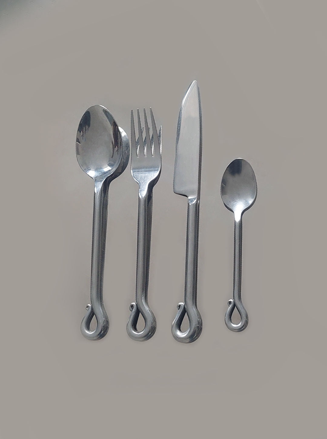 The "Vintage Set of 4 Twist Cutlery" by Les Objoies, featuring stainless steel tablespoon, fork, knife, and teaspoon with twisted loop handles, is arranged in a row against a plain gray background.