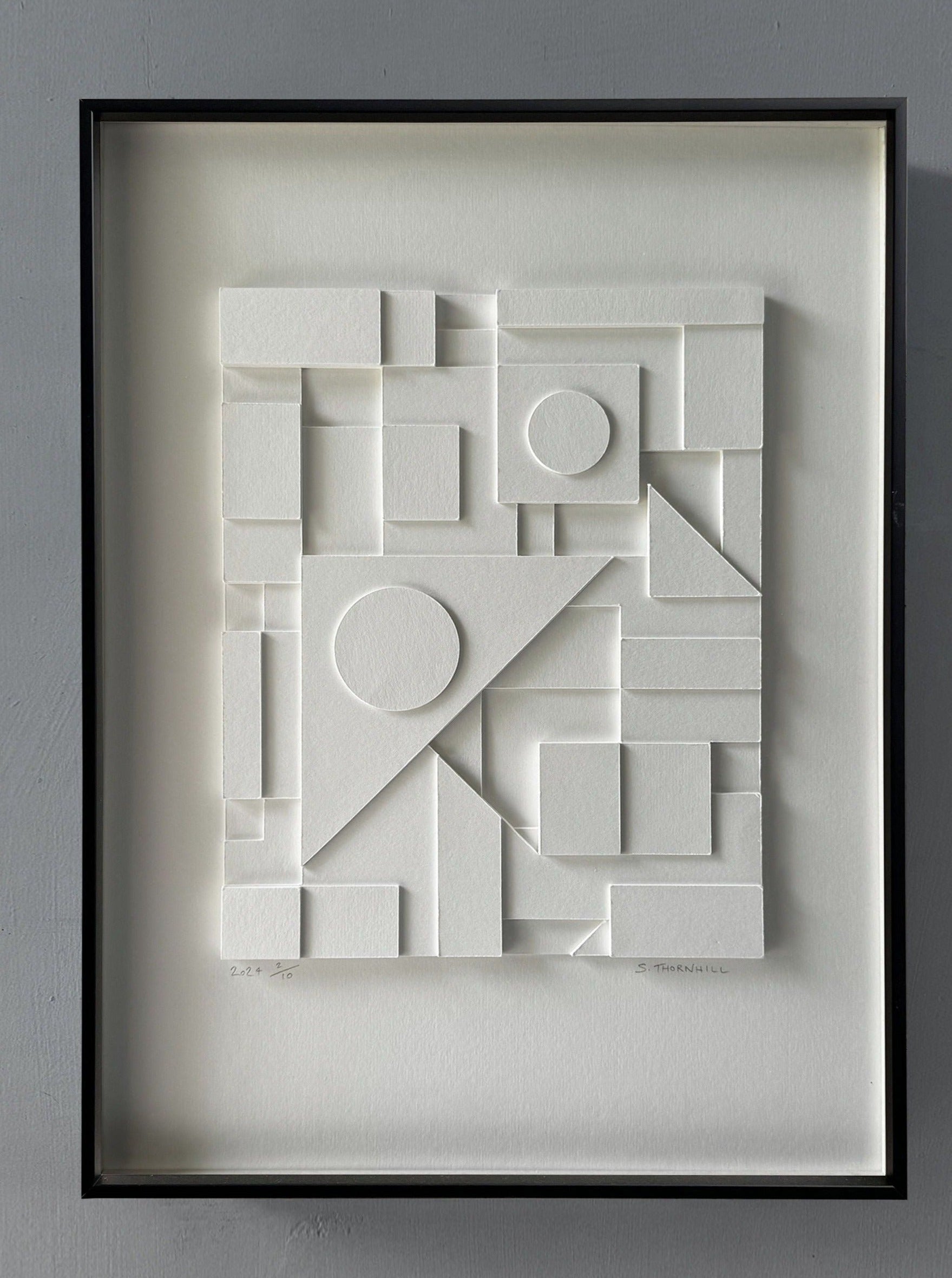 A framed piece of minimalist art, **Composition124** by **Sean Thornhill**, features a handmade geometric composition made of three-dimensional white shapes, including circles, rectangles, and triangles, arranged in a balanced and intricate pattern on a white background. This limited edition paper relief adds an elegant touch to any space.