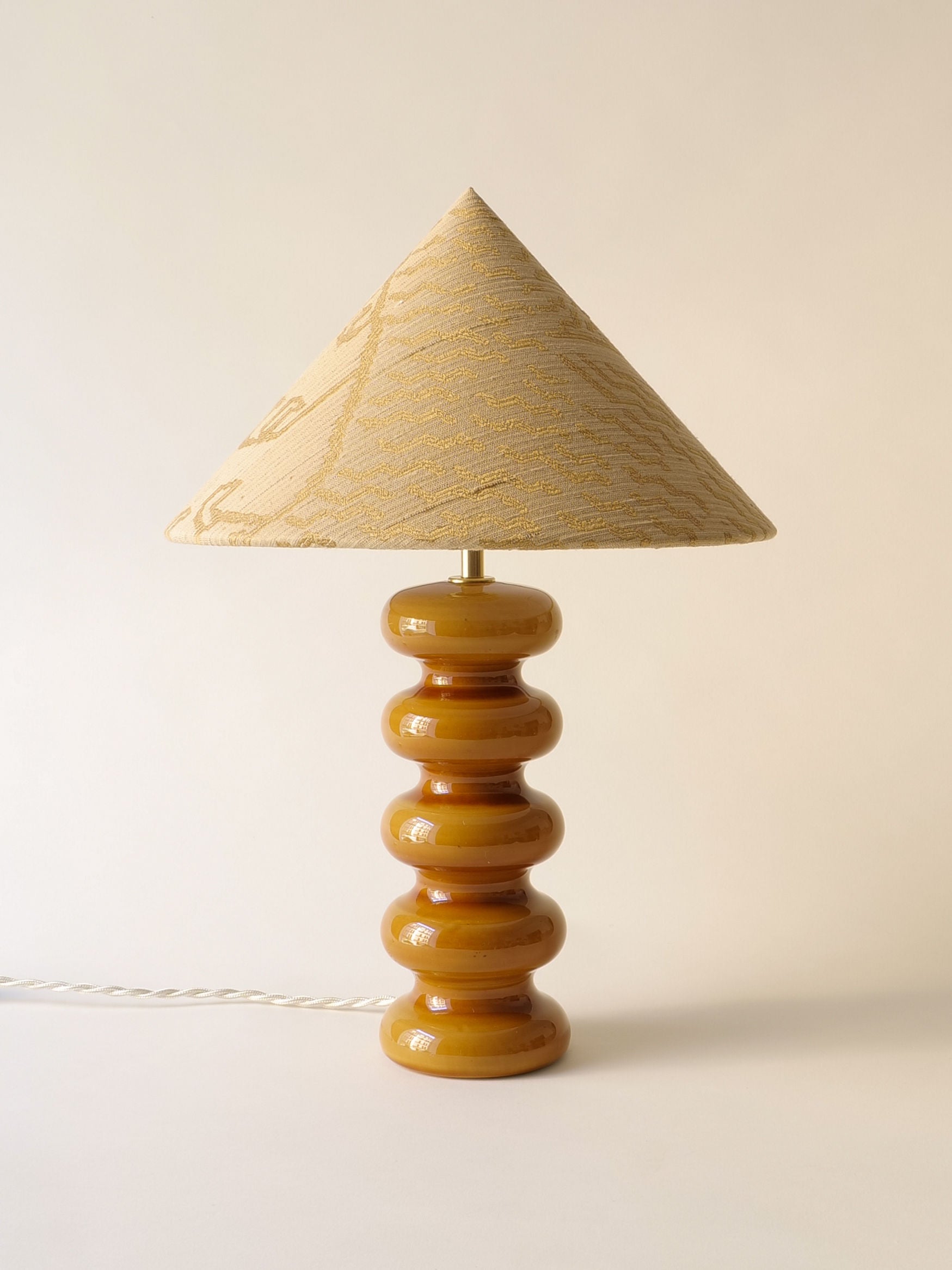 The Sculptural Ceramic Lamp from Collection apart features a textured beige conical shade on a glossy mustard stacked circular base, echoing Doulton England's elegance and standing out beautifully against a plain white backdrop.