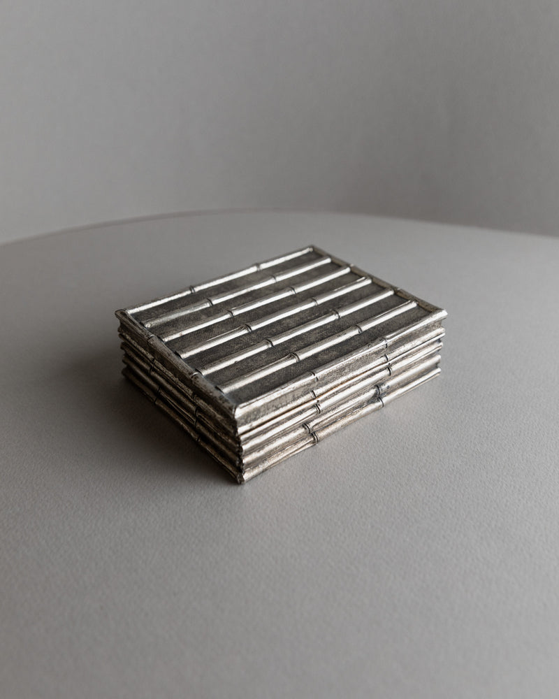 A neatly arranged stack of rectangular, ribbed, silver-plated vintage boxes by Bottega Jacobs, France 1970s, evokes a retro chic vibe. They rest flat on a smooth, neutral surface against a plain background.