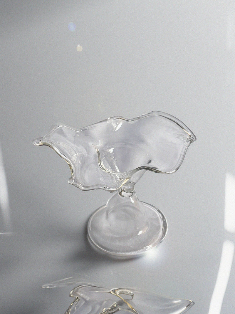 The 'Myth' Ashtray by Pia Glassworks is a unique, abstract glass piece with a fluid wave-like form on a reflective surface. Handcrafted with an irregular, organic shape and mounted on a rounded base, it casts subtle reflections—a decor item as captivating as bespoke art.