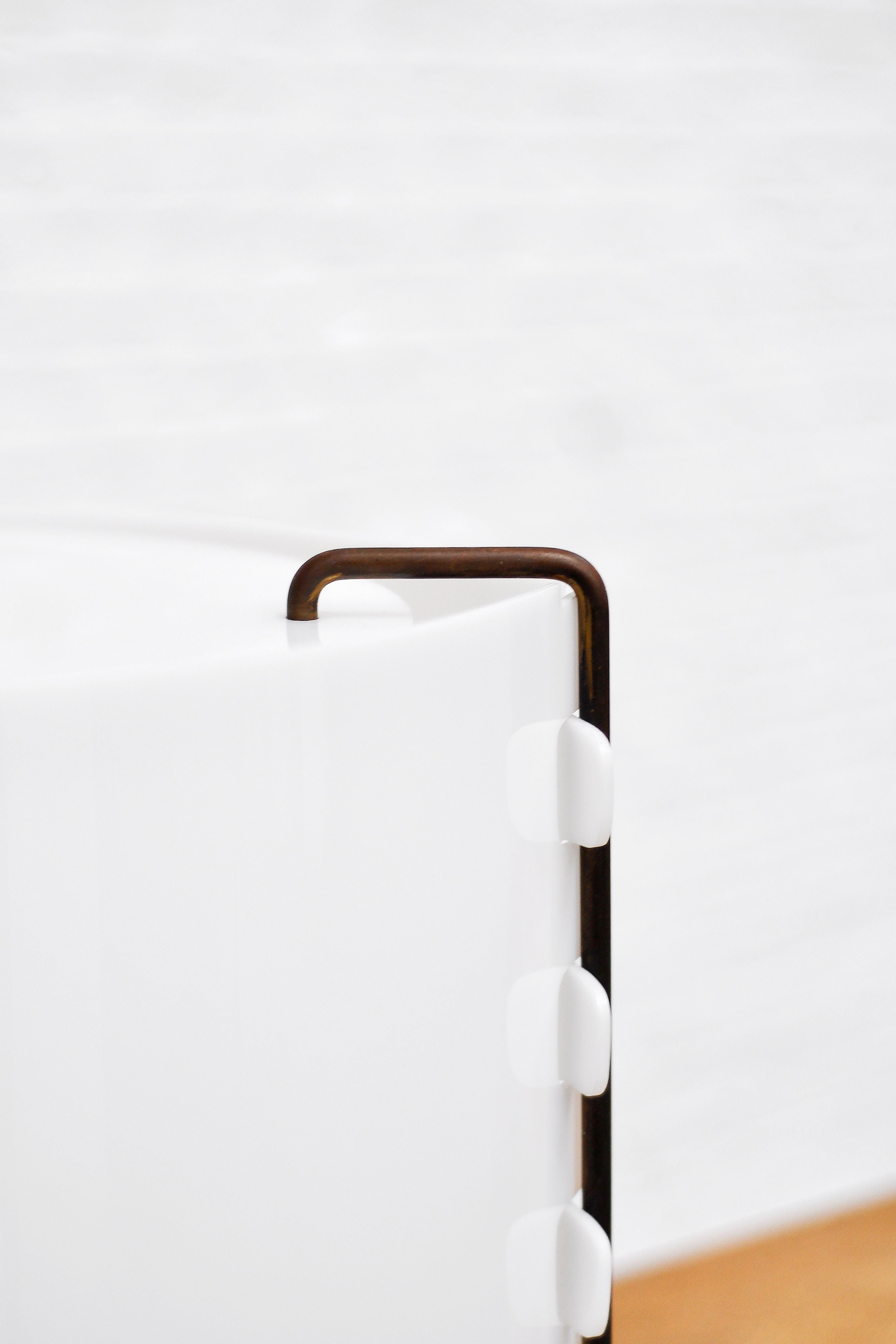 Close-up of a white rounded 'M8 Fanal' lamp corner by Joseph-André Motte for Huchers-Minvielle, featuring a metal handle. The ribbed edge reflects French mid-century modern style, while the blurred background emphasizes its sleek design akin to a Joseph-André Motte piece from 1958. Brand: Introverso.