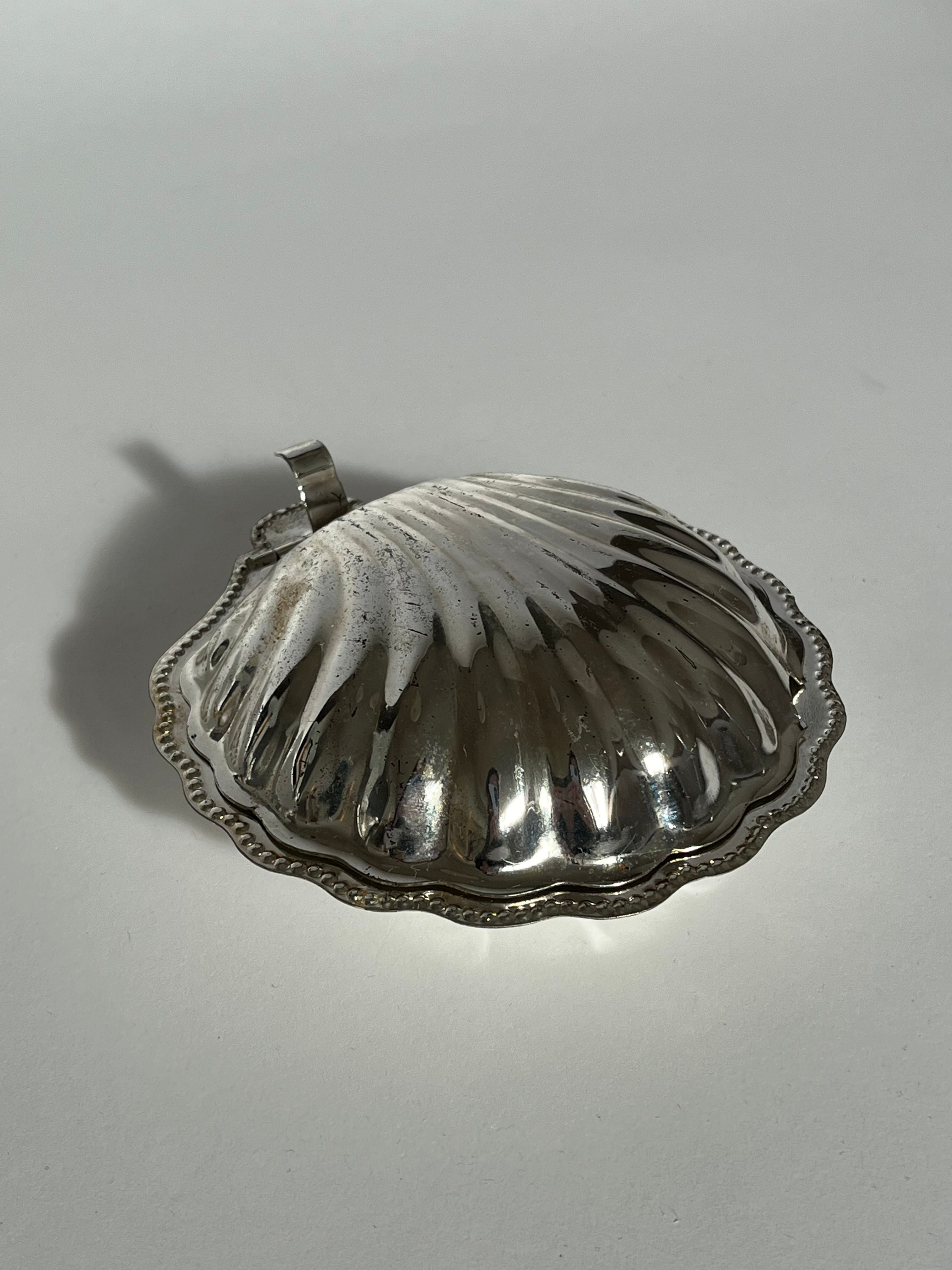 The Shell Shaped Butter Dish by septembre studios, featuring a ridged pattern and scalloped edge reminiscent of a vintage brass seashell, sits elegantly on a plain white surface.