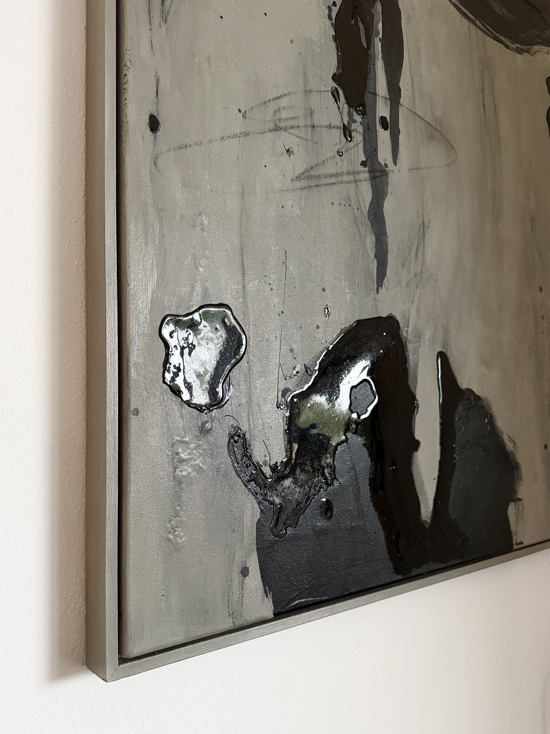 This detailed view shows "Black Drift," an abstract painting by STUDIOPOLS, displayed on a framed canvas. The piece utilizes acrylic paint to create glossy, elevated black spots and irregular shapes against a smooth, muted gray background. An elegant thin gray frame encloses the artwork.