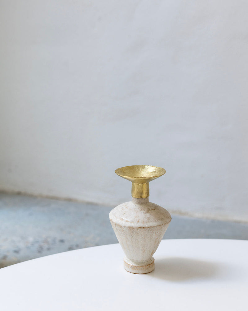 The Isolated n.6 Vase by Canoa Lab, featuring white textured ceramic inspired by Mediterranean design and a wide gold metallic rim, rests on a round white surface against a plain light gray background.