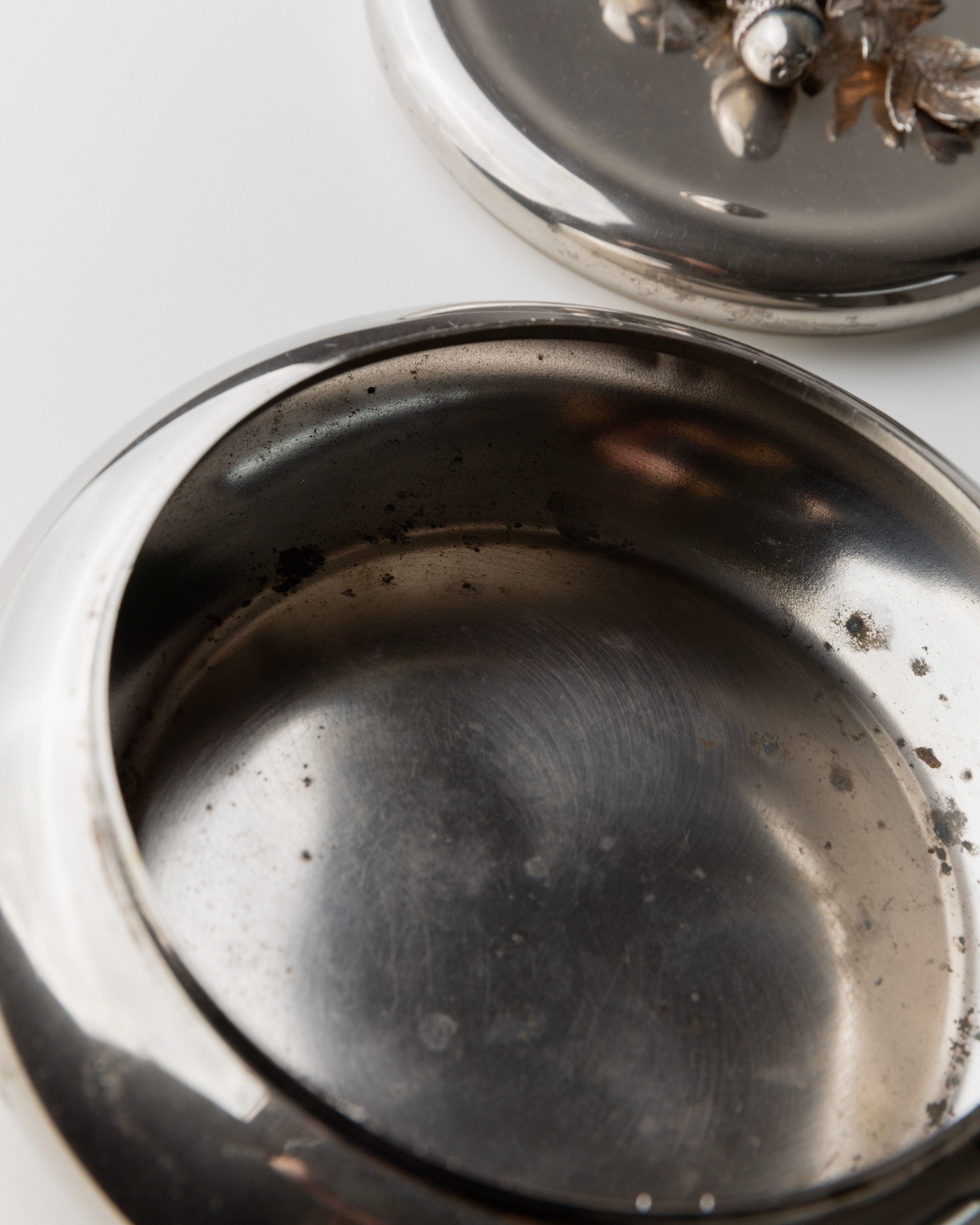 Close-up of a Bottega Jacobs' 1950s Italy silver-plated box. The partially visible lid shows an ornate floral design with an acorn handle. Its tarnished interior is empty, displaying wear signs.