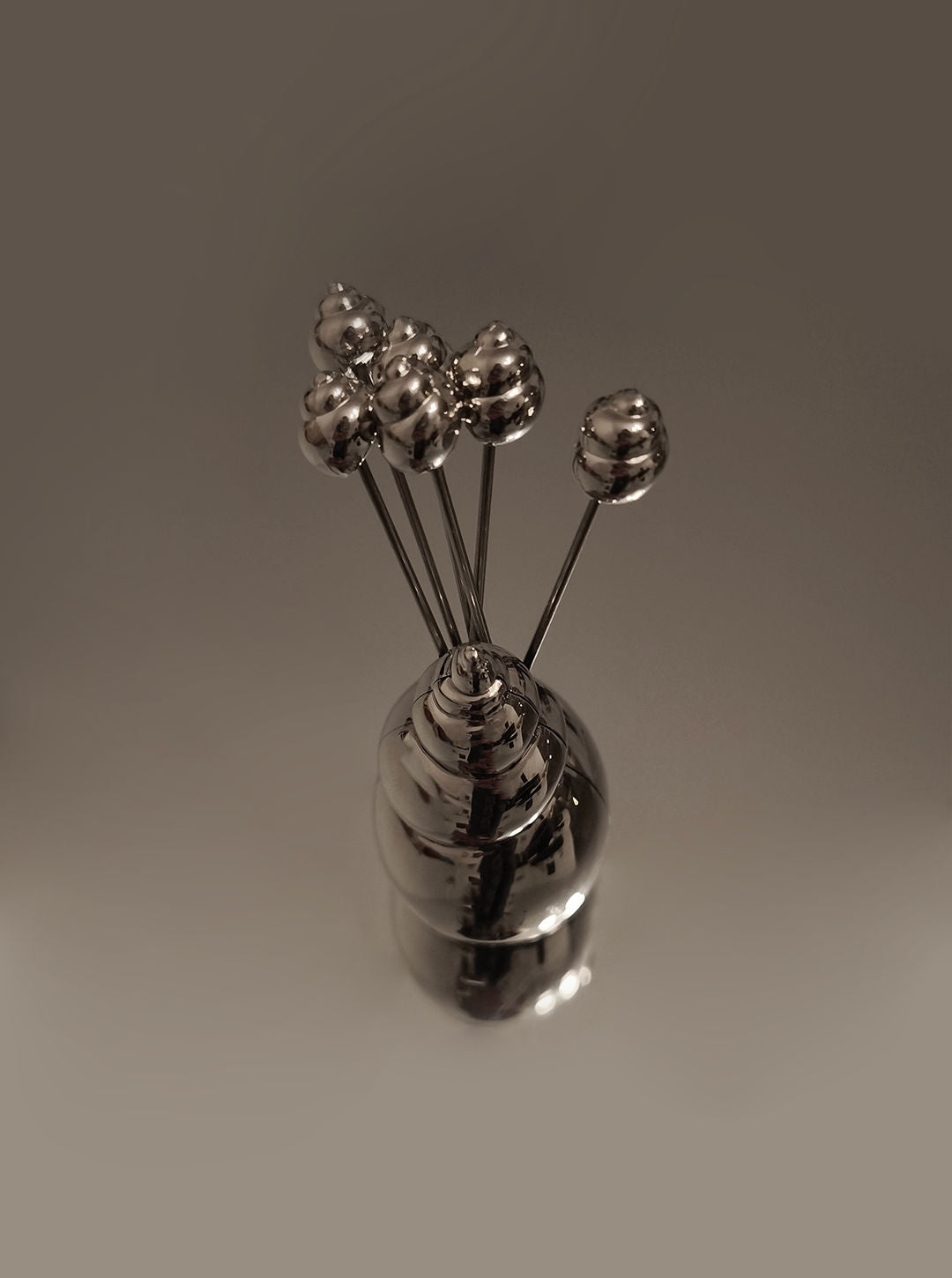 The Les Objoies Shell Cocktails Picks set features a metallic, spiral holder with cocktail picks, each topped with a small sphere, displayed against a soft brown background.