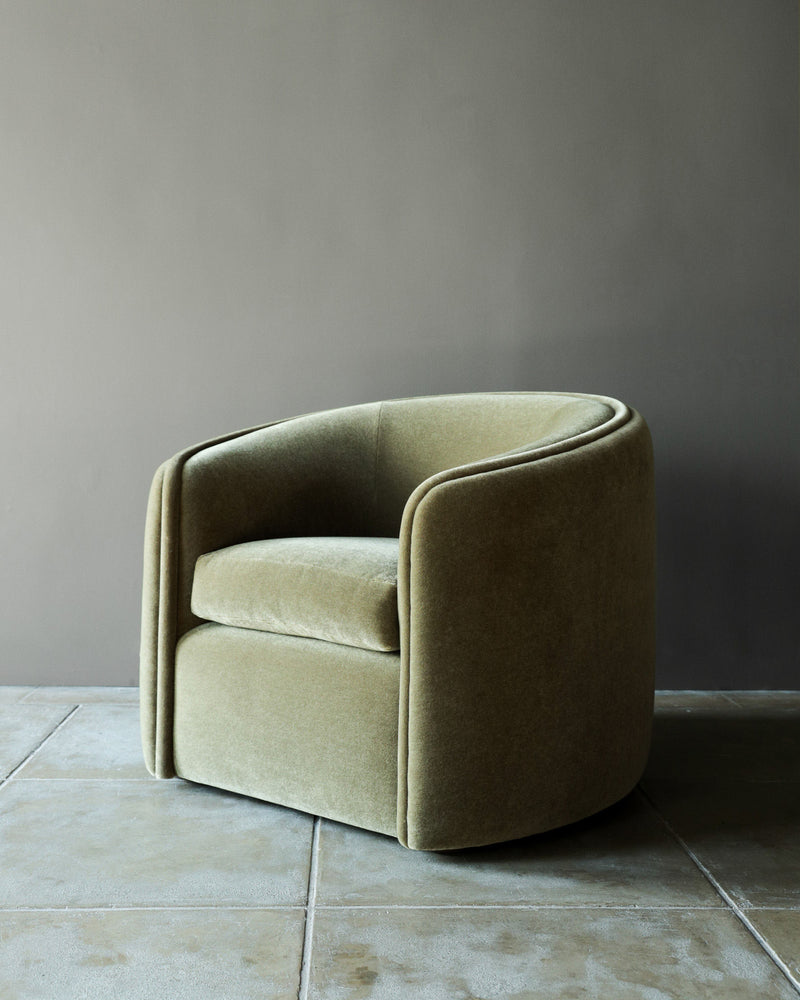 The 'DE GAULLE' Mohair Armchair by Studio OSKLO features rounded arms and back in olive-green velvet, exuding bespoke craftsmanship and refined French mid-century elegance against a taupe wall on a tiled floor.
