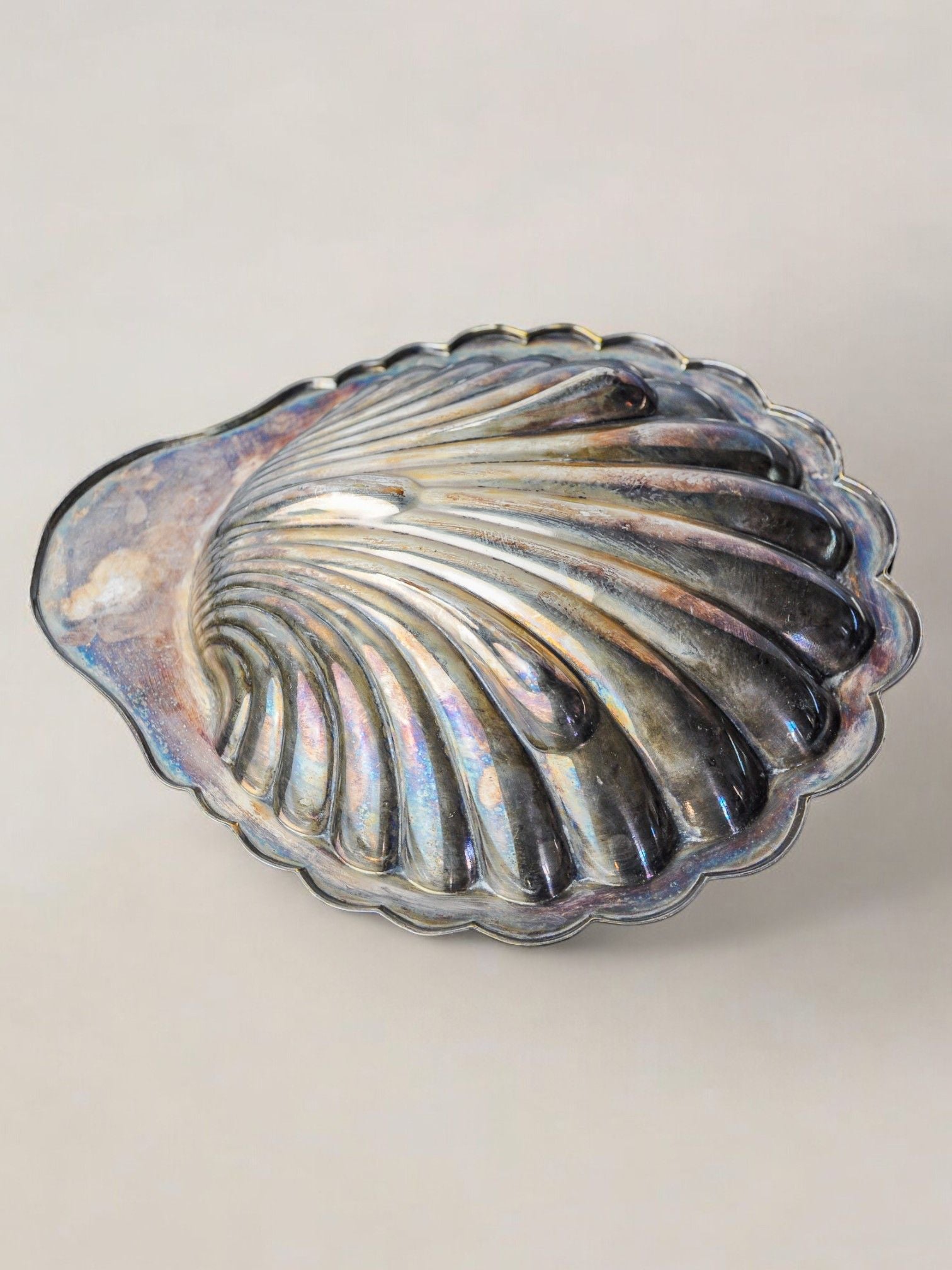 A Large Shell Shaped Vide-Poche by Malamar Studio, created in Italy in 1970, sits on a light surface. This metallic piece features ribbed textures and an iridescent glossy finish, displaying shades of blue, purple, and gold.