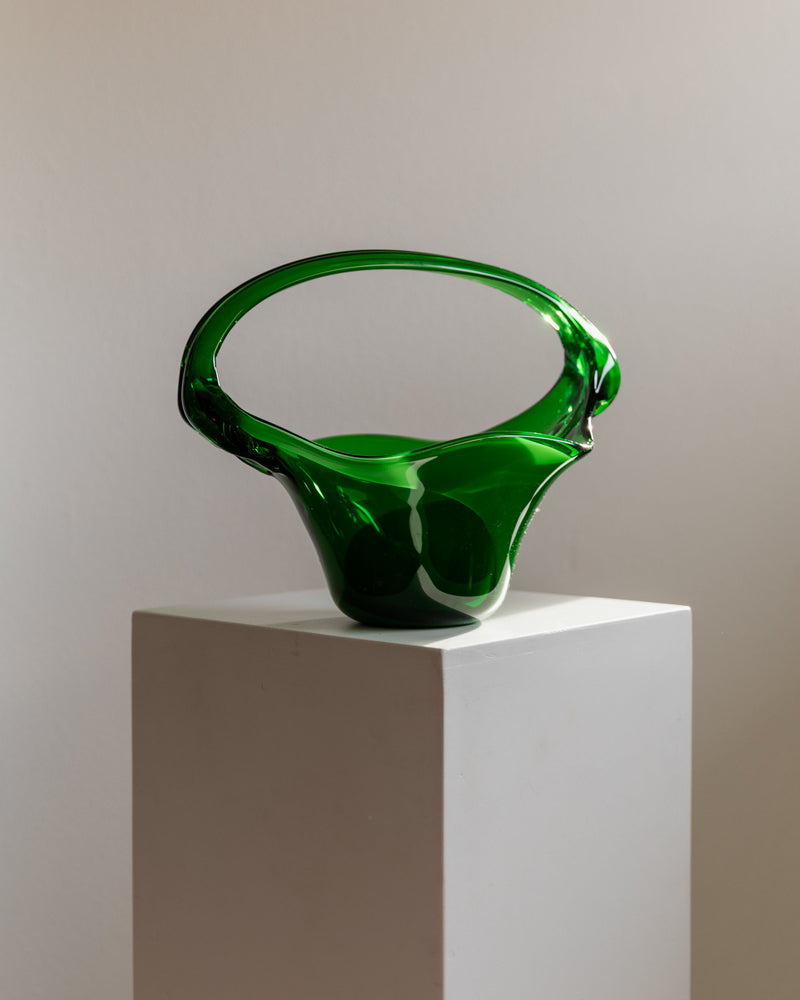 The Murano Glass Handle Bowl 70s by Bottega Jacobs features a sleek, modern, green glass design with an abstract looped shape. Displayed on a simple white pedestal against a neutral background, it's the perfect statement piece for any art enthusiast's collection.