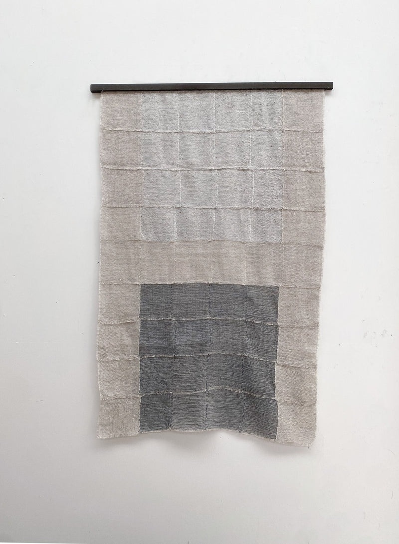 The "Blue Sky" Artwork by Sundance Studio is a woven wool-cotton wall hanging with a grid pattern and a prominent gray rectangle at the lower center, displayed on a rod against a plain white wall.