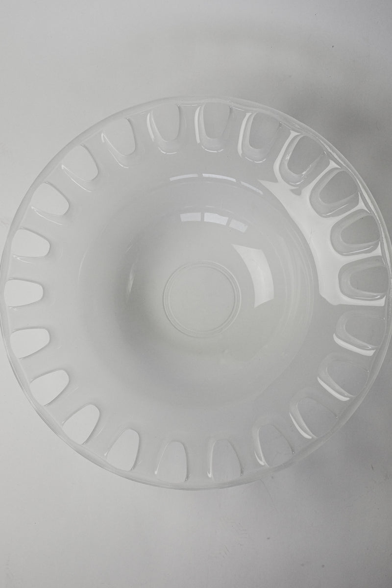 A glossy, transparent XL bowl named "Large Bowl of Milk Glass" by septembre studios features a wide rim and evenly spaced oval cutouts around the edge, photographed from above on a plain white background.