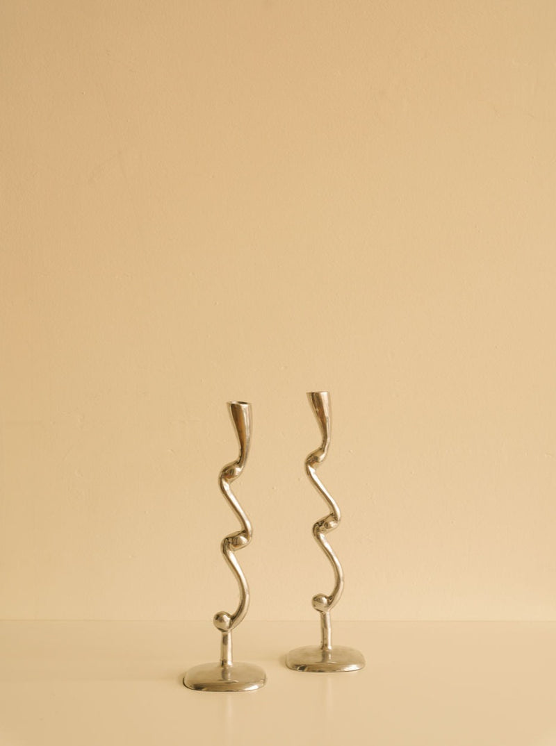 Two Curly Candleholders from Les Objets Amsterdam against a plain beige background.