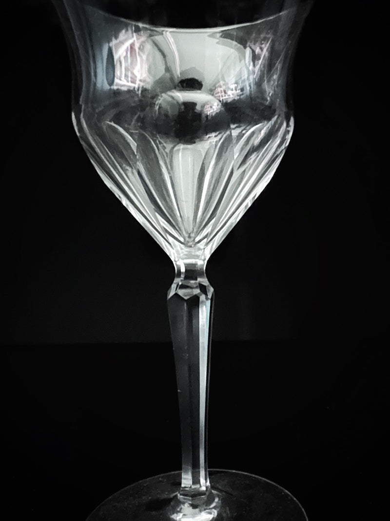 A set of 9 hand-cut crystal wine glasses from the 1960s by Dodo Vintage stands against a dark background, showcasing the artistry of fine craftsmanship. Light dances across their surfaces, highlighting the elegant geometric pattern and exquisite design.