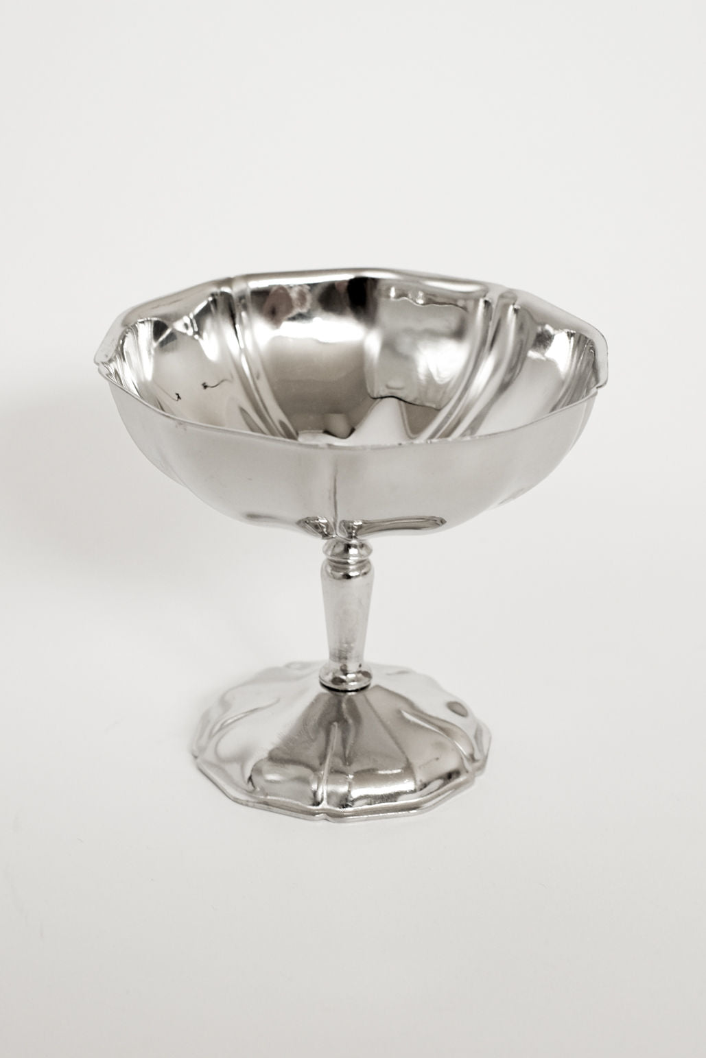 A set of six shiny, stainless steel ice coupes by septembre studios, each with a fluted edge and decorative base, displayed against a plain white background for vintage appeal.